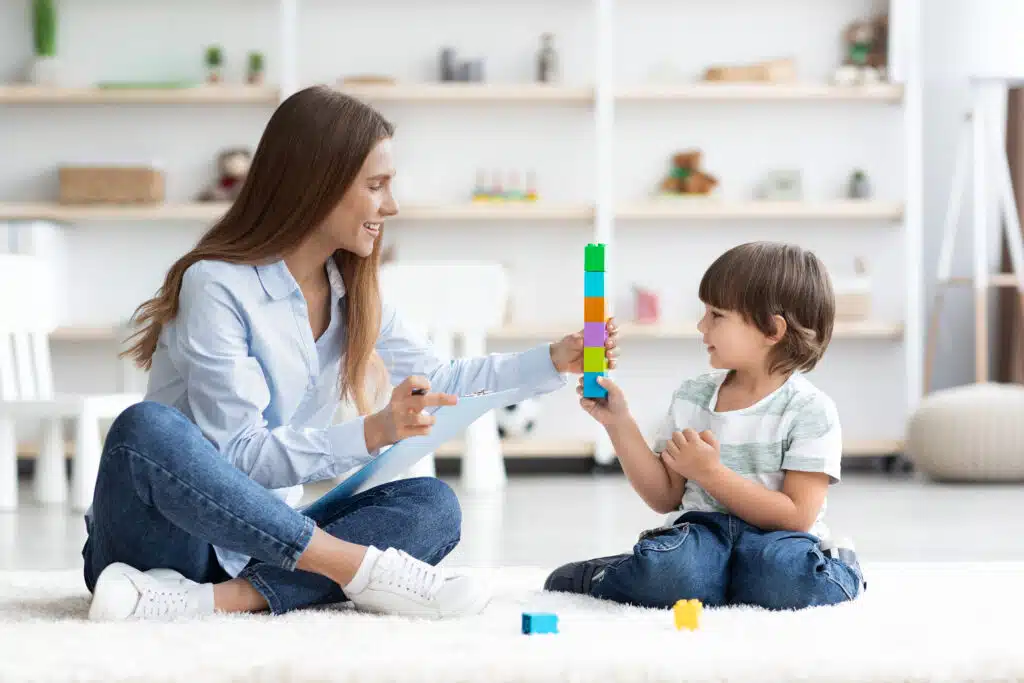 Terapeuta e criança sentados no chão interagindo com brinquedos coloridos